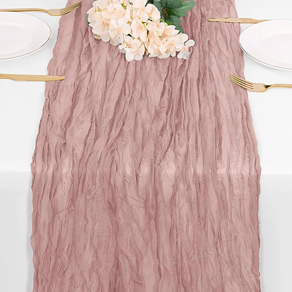 A dusty rose burgundy cheesecloth table runner with white flowers and gold cutlery.