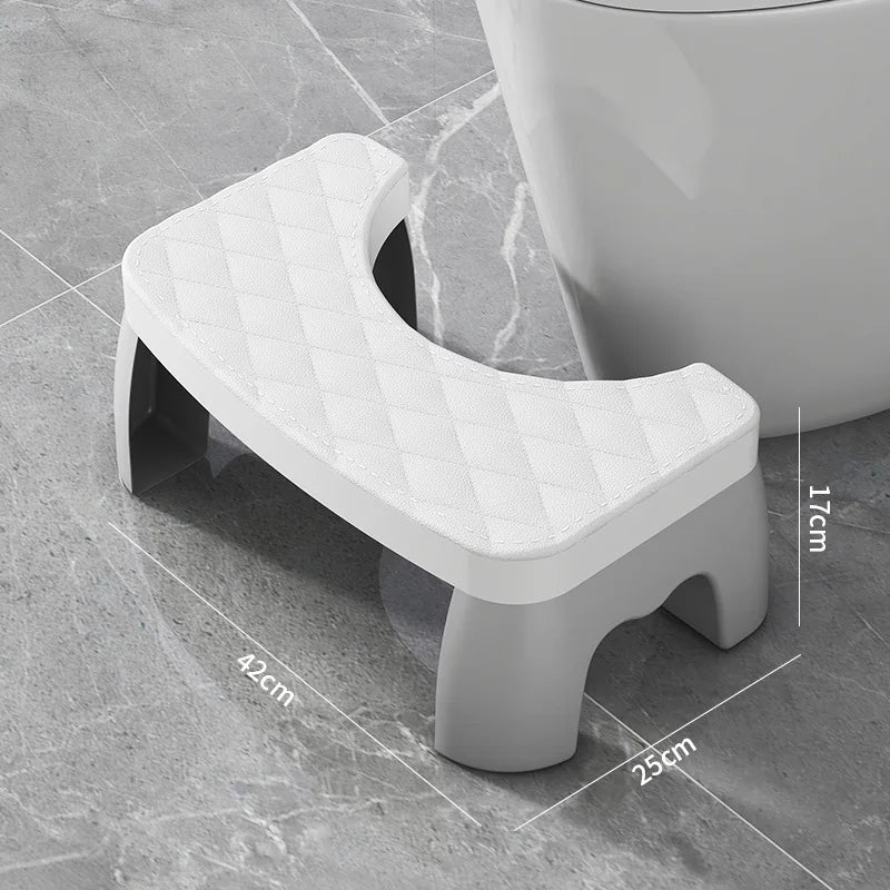 A white adjustable adult toilet squat stool with a diamond-patterned seat is shown on a gray tiled floor.