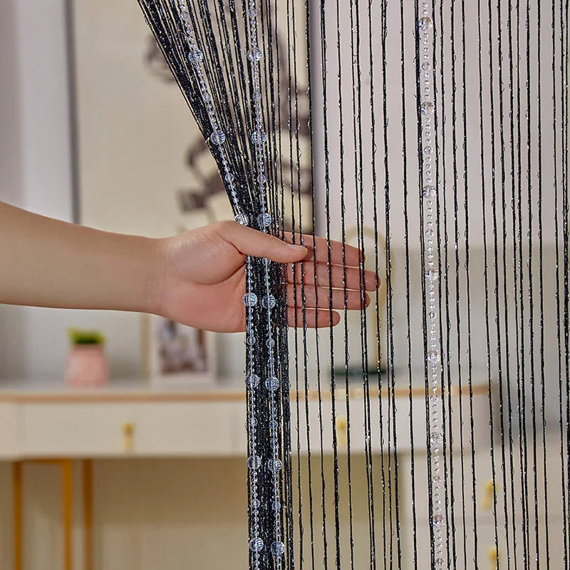 A hand is touching a sheer black and clear crystal beaded string curtain fabric.
