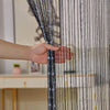 A hand is touching a sheer black and clear crystal beaded string curtain with tassels.