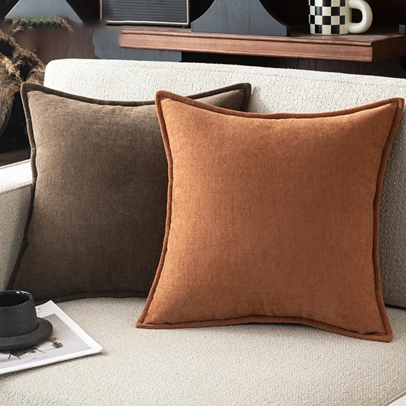 A close-up of a rust brown chenille throw pillow resting on a light beige sofa.