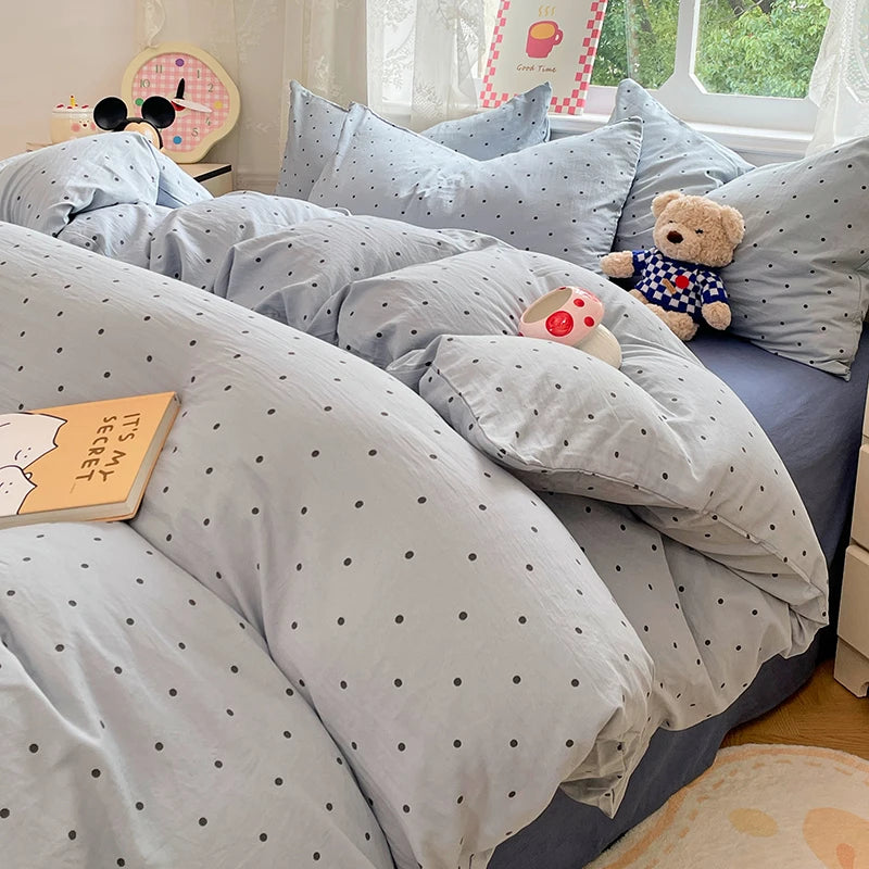 A bed covered with a light blue polka dot duvet and pillows, featuring a teddy bear and a book.
