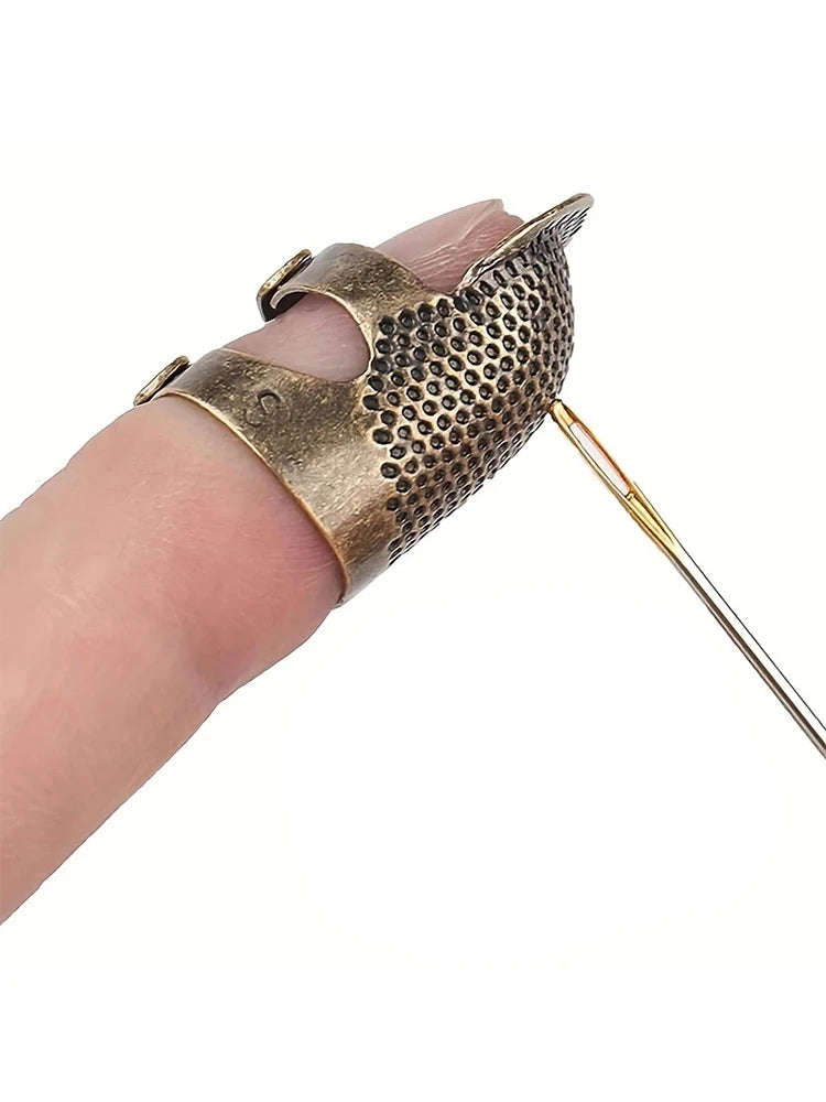 A hand holds an antique sewing thimble and needle protector set with a textured metal thimble and a thin needle.