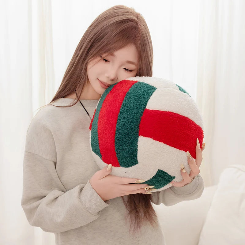 A woman holds a red and green plush volleyball ball cushion against her face.