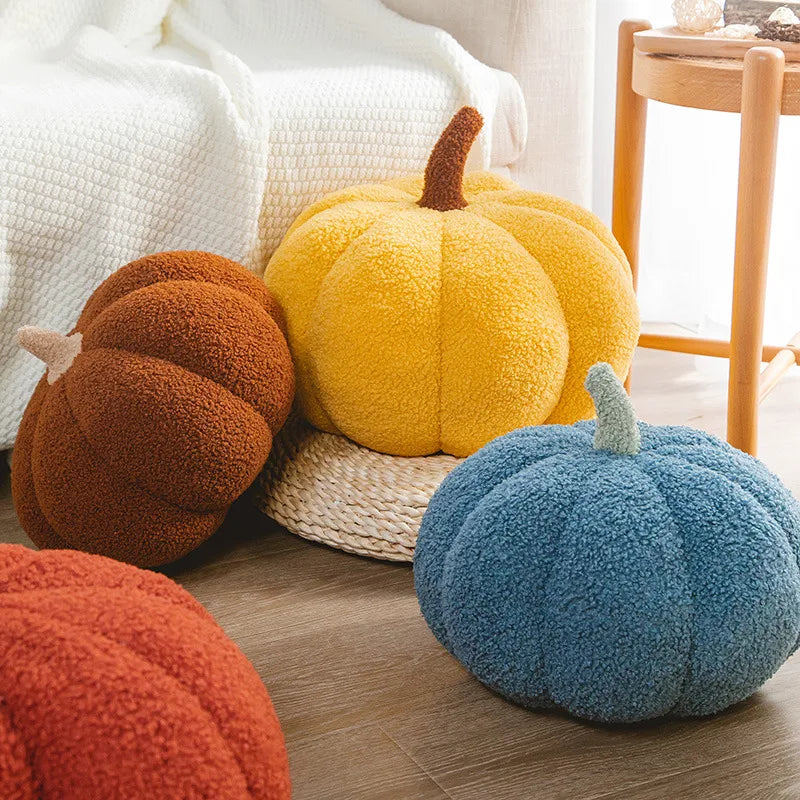 A collection of fuzzy plush pumpkins in orange, yellow, and blue resting on a wooden surface.