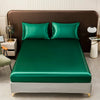 A solid emerald green satin bedding set displayed on a bed with brown upholstery and white nightstands.