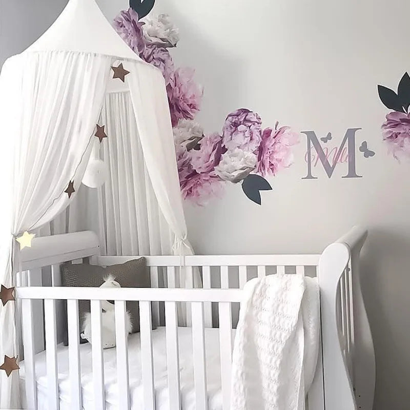 A white crib decorated with a pink floral canopy and mosquito net for a baby