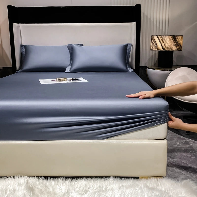 A fitted sheet and pillow set in slate gray is displayed on a bed with a white headboard and light-colored frame.