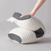 A hand is adjusting a beige quilted neck pillow with gray accents on a light gray background.