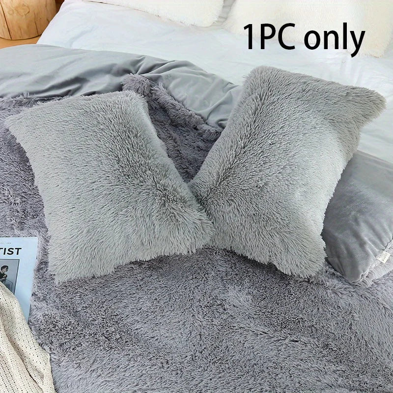One piece of gray faux fur pillow covers resting on a bed with a gray blanket.