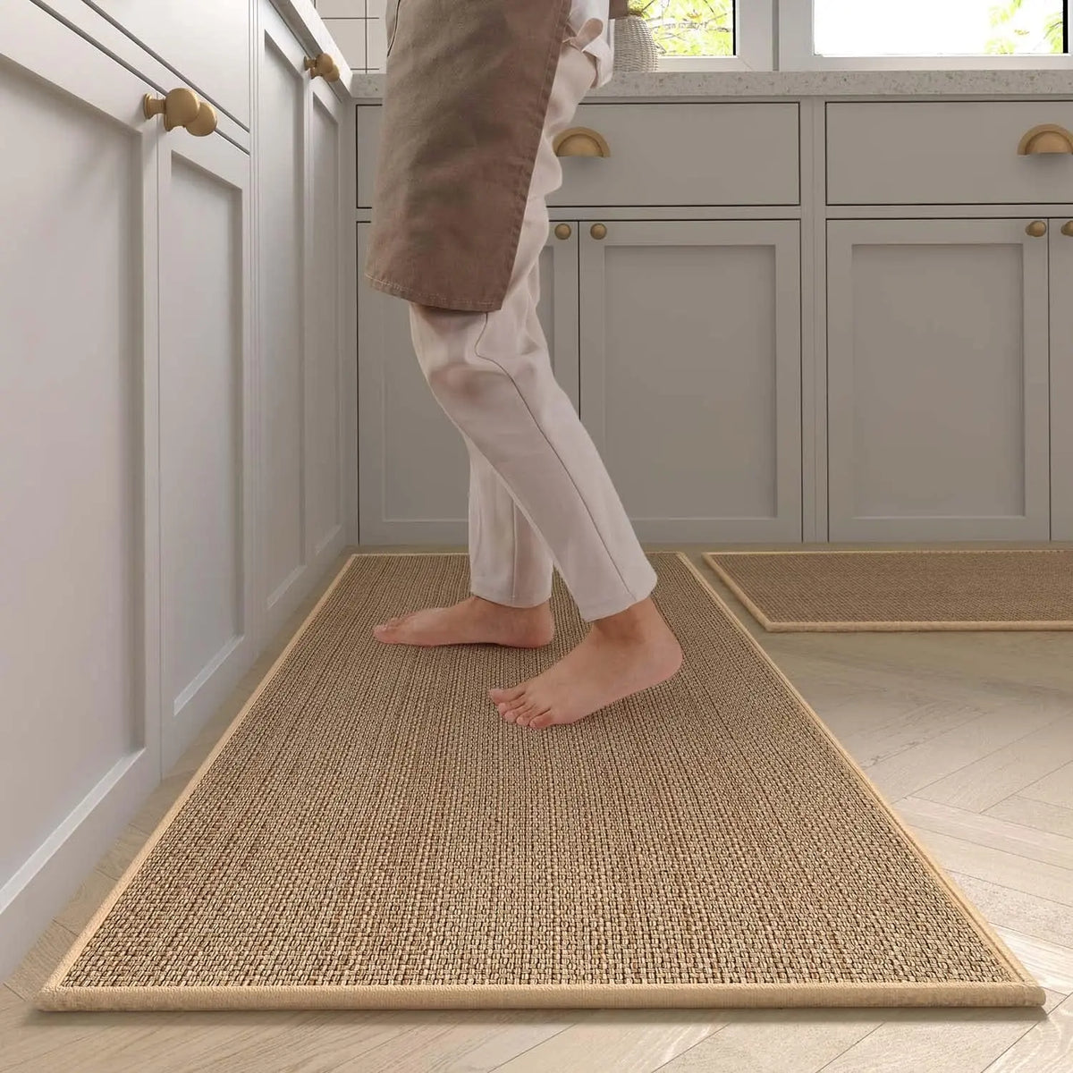 A light brown faux sisal kitchen rug placed on a light wood floor in a modern kitchen setting.