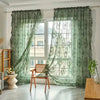 A pair of sheer green lace floral window curtains hanging in a bright room.