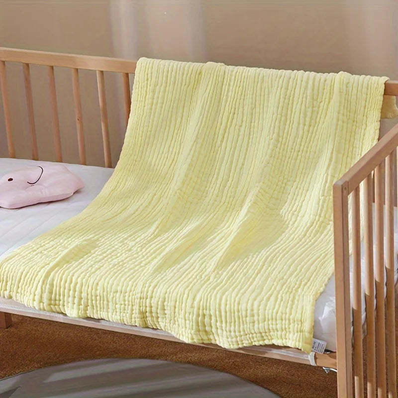 A bright yellow, textured 6-layer cotton gauze blanket draped over a wooden crib railing.