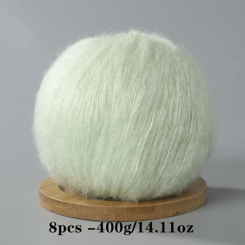A ball of light mint green mohair yarn for crafting displayed on a wooden base.