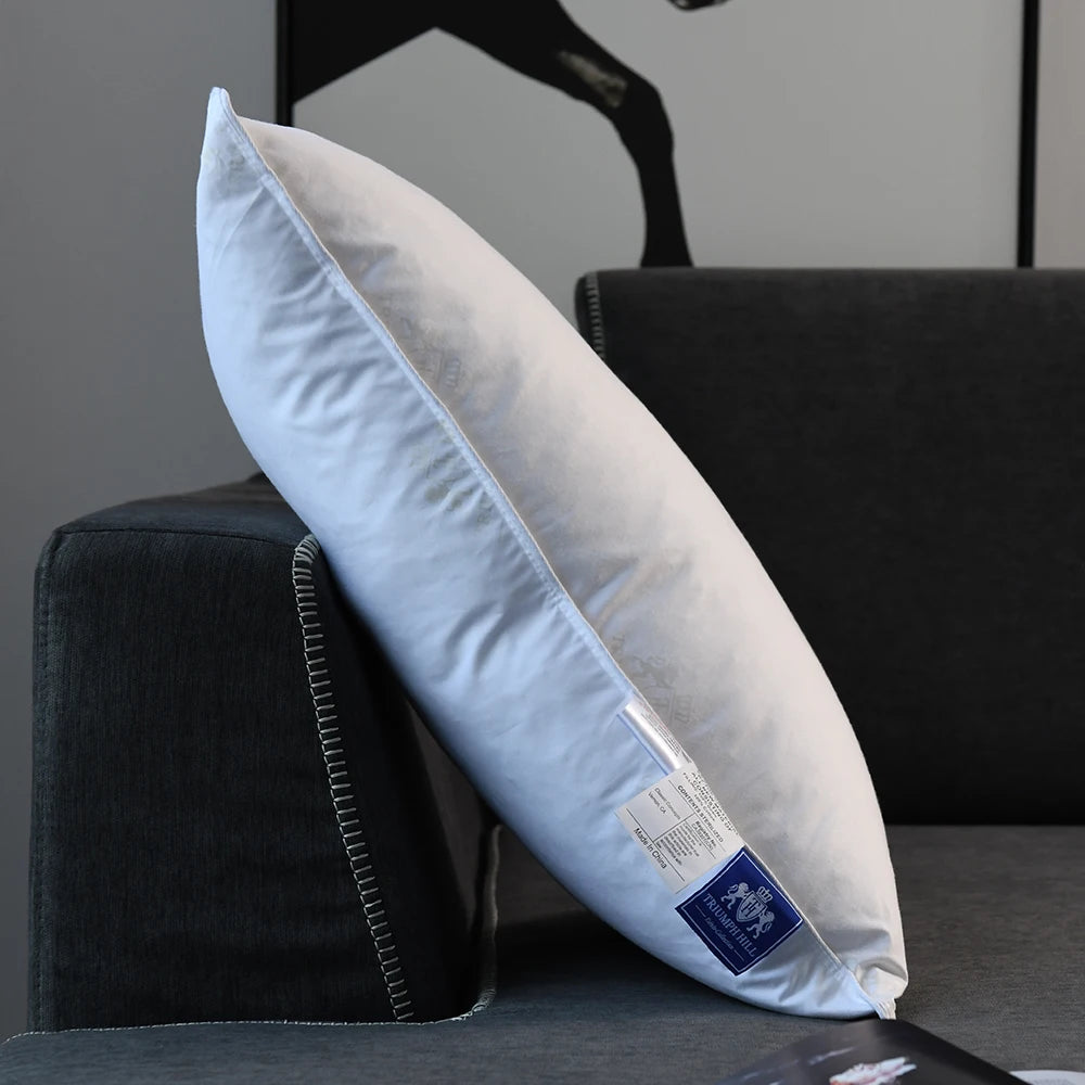 A white luxury goose down and feather pillow resting on a dark surface next to a black cushion.