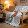 A striped throw blanket featuring a C-Curious George character on a light beige sofa.