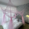A large four-door mosquito net draped over a bed in a room with gray patterned wallpaper and sheer curtains.