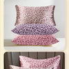 A stack of five leopard print satin pillowcases in various shades of pink and purple.
