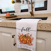 A white kitchen towel with a fall pumpkin print hanging on a cabinet door.