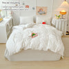 A white duvet cover, pillowcases, and decorative items are displayed on a bed with a light-colored wooden frame.