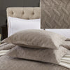 A set of beige embroidered cotton quilted pillow covers and a cream-colored tufted pillow shown on a bed.