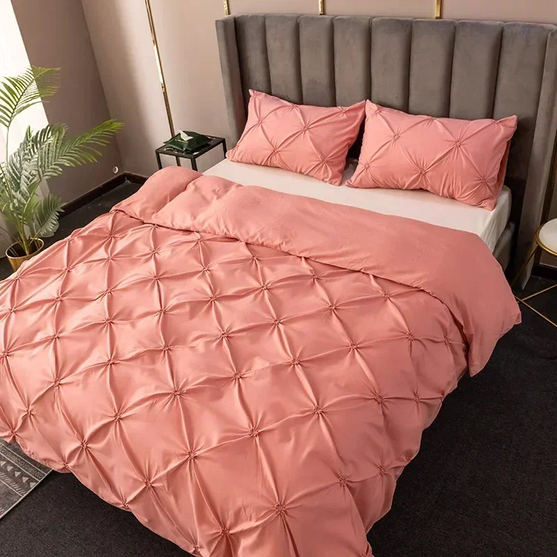 A pink 3D pinch pleated duvet cover set displayed on a bed with a gray upholstered headboard.