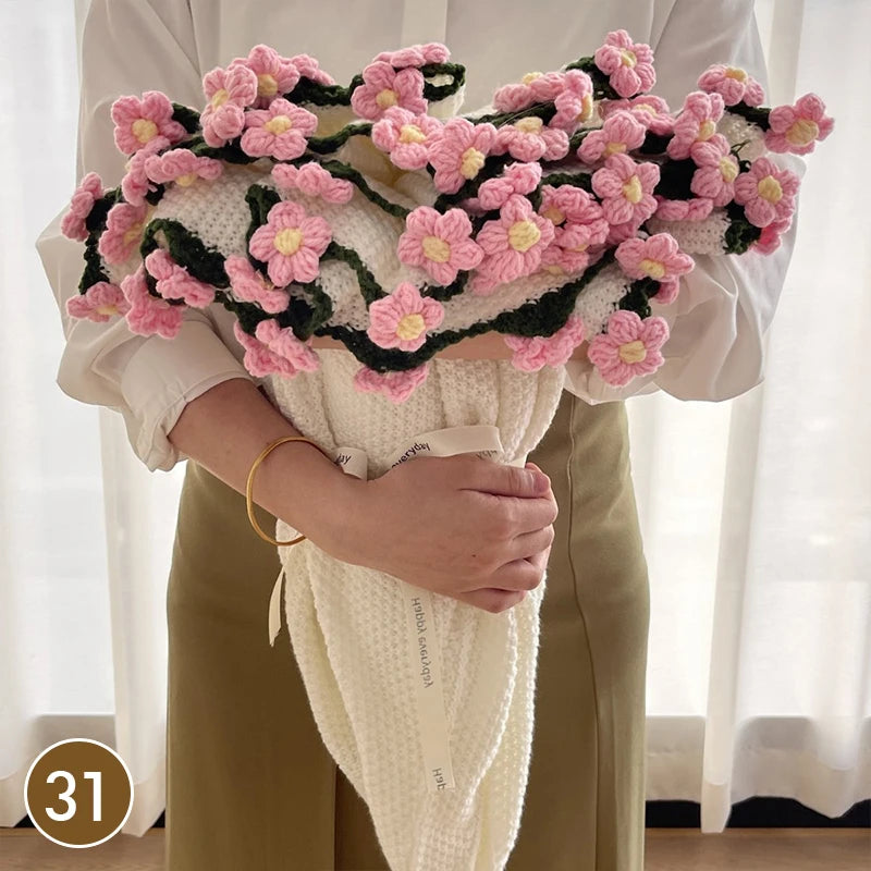 A hand knitted floral rose bouquet throw blanket in pink and green is held by a person.