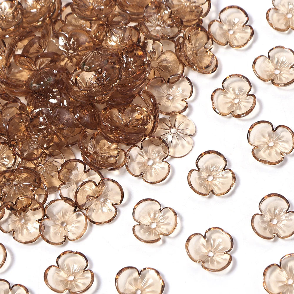 A close-up of small, translucent amber resin flower bead caps for jewelry making scattered on a white surface.