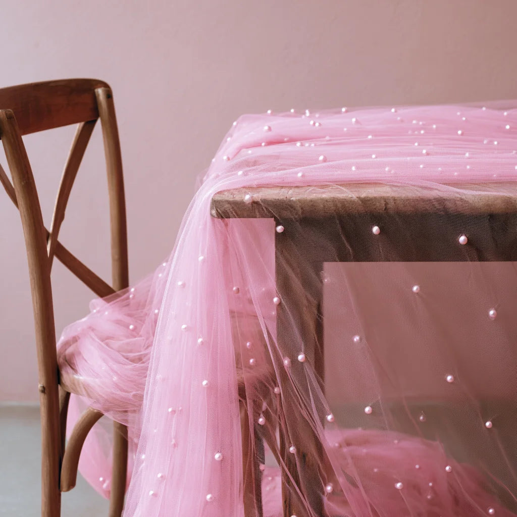 A pink pearl tulle table runner draped over a wooden table.