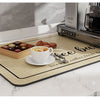 A wooden mat with coffee beans and treats is placed on a white marble countertop next to an espresso machine.