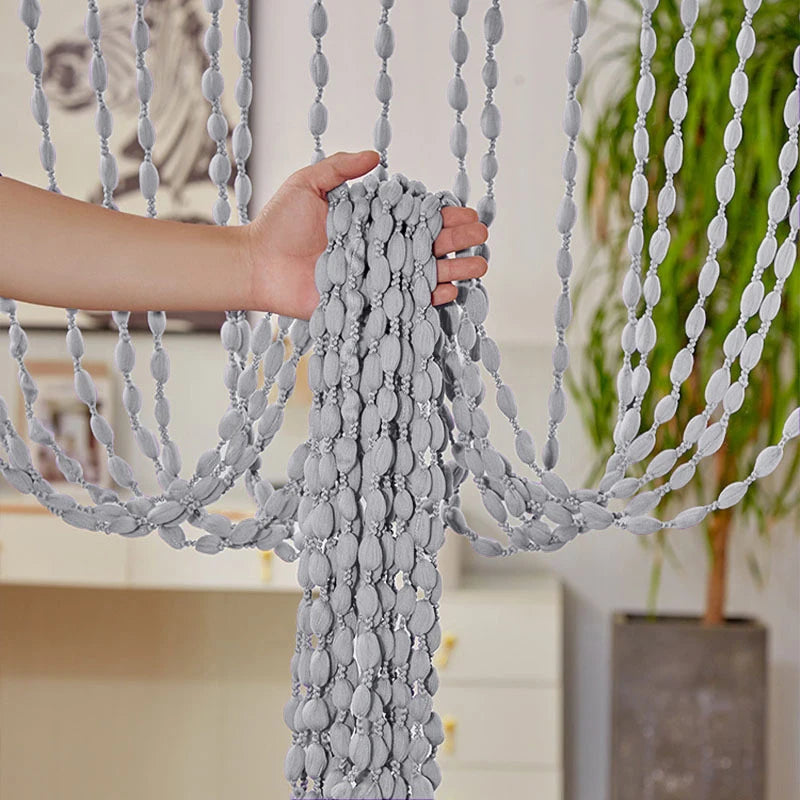 A hand is holding a gray decorative fabric door curtain with tassel trim.
