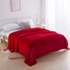 A vibrant red coral fleece throw blanket draped over a white bed in a bright room.