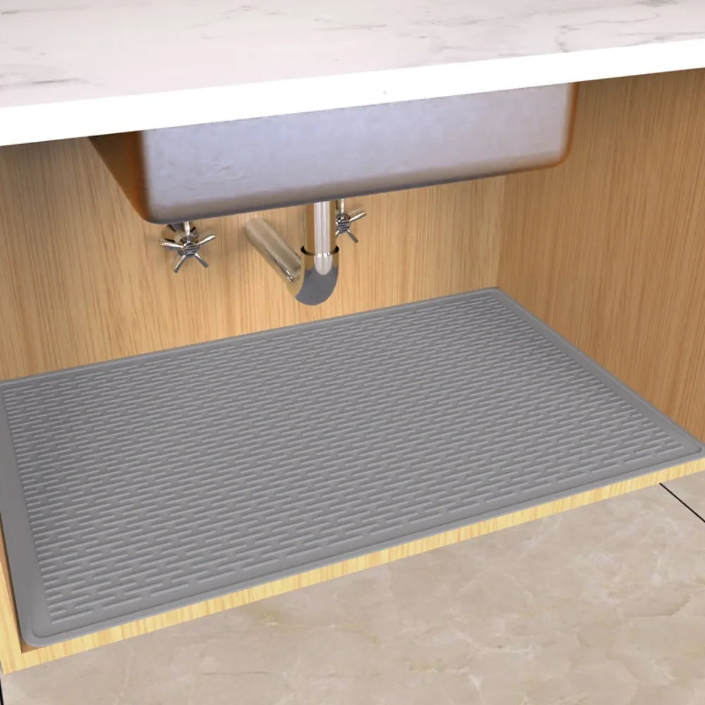 A gray silicone mat is placed inside a wooden under sink cabinet for drainage and protection.