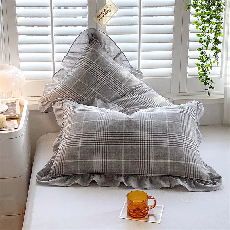 A set of two soft plaid washed cotton pillowcases with ruffled edges resting on a white surface.