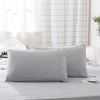 A set of two light gray soft polyester pillow covers displayed on a bed with a white checkered curtain backdrop.