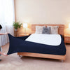 A dark navy high-stretch elastic box spring cover is shown on a wooden bed frame with fluffy pillows.