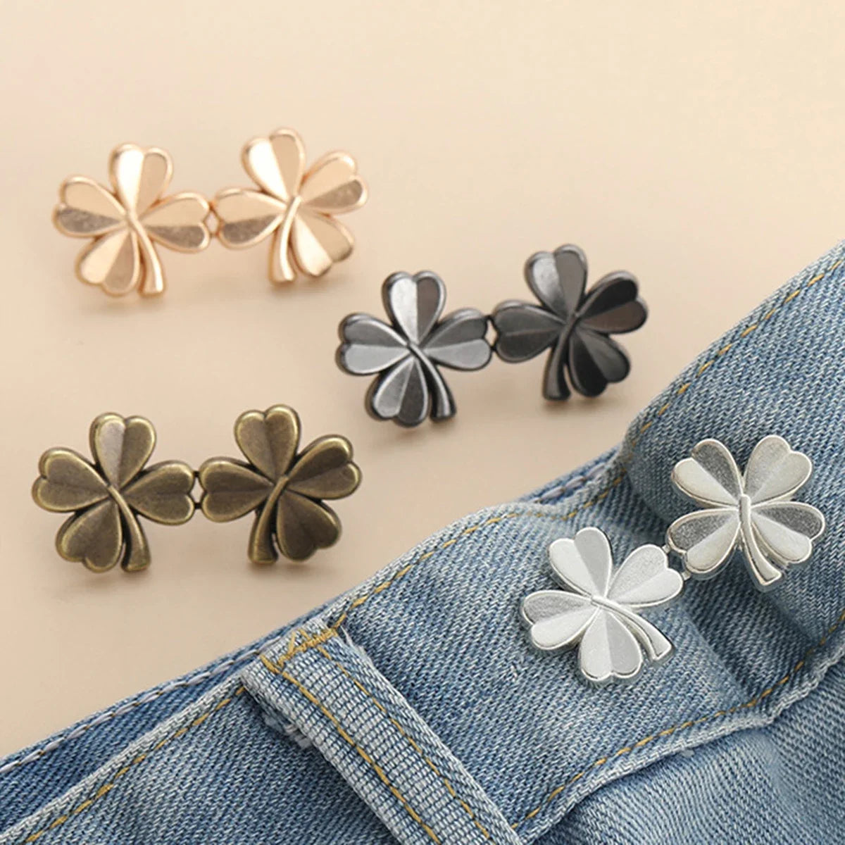 A collection of adjustable button clips in gold, silver, and bronze tones shown against a denim fabric.