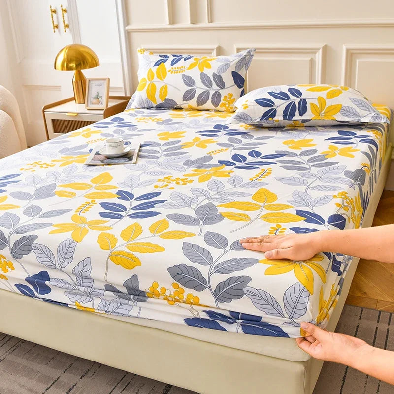 A floral fitted sheet set with blue and yellow leaves is displayed on a bed, being touched by a hand.