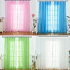 Three sets of sheer tulle curtains in pink, blue, and green hanging in a window.