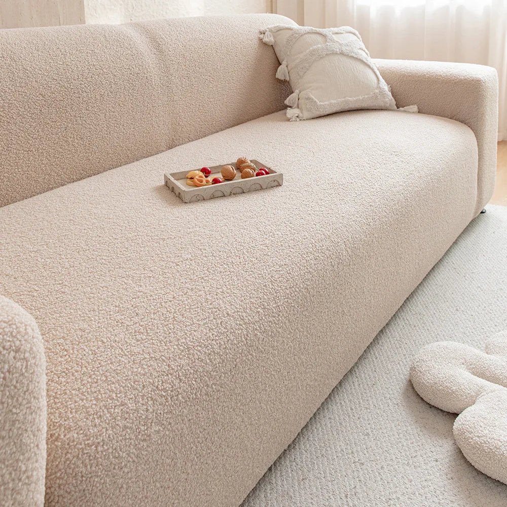 A light beige jacquard velvet sofa cover with decorative pillows and a fruit tray on the seat.