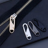 A set of detachable metal zipper pullers and a zipper slider on a dark fabric background.
