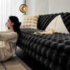 A person is relaxing on a dark gray plush velvet sofa cover with a light beige throw pillow and a gold light fixture in a mod