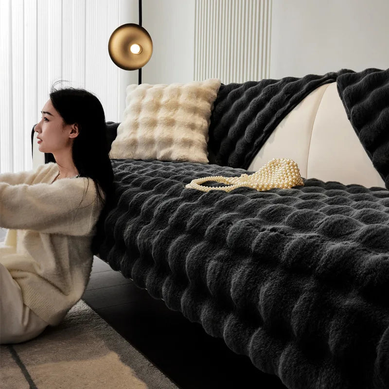 A person is relaxing on a dark gray plush velvet sofa cover with a light beige throw pillow and a gold light fixture in a mod