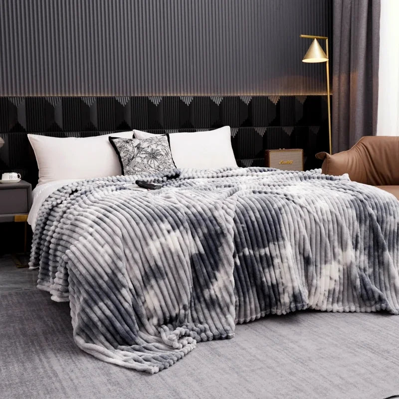 A gray tie-dye flannel fleece throw blanket draped over a bed in a modern bedroom setting.