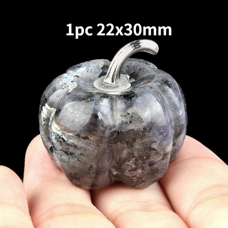 A smooth, grey natural stone pumpkin figurine with a silver stem is held in a person's hand.