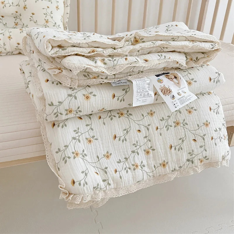 A stack of white muslin blankets with a floral print are displayed on a light-colored surface.