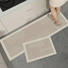 A rectangular beige non-slip kitchen floor mat is placed on a gray tile floor next to a white cabinet.