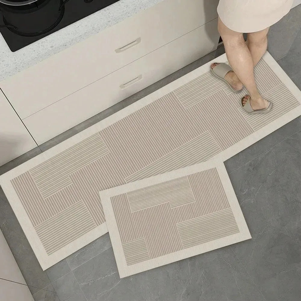 A rectangular beige non-slip kitchen floor mat is placed on a gray tile floor next to a white cabinet.