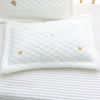A white quilted pillow with gold stars and blue crescent moons resting on a white textured surface.