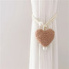 Cream colored plush heart tiebacks tied onto a white curtain fabric.
